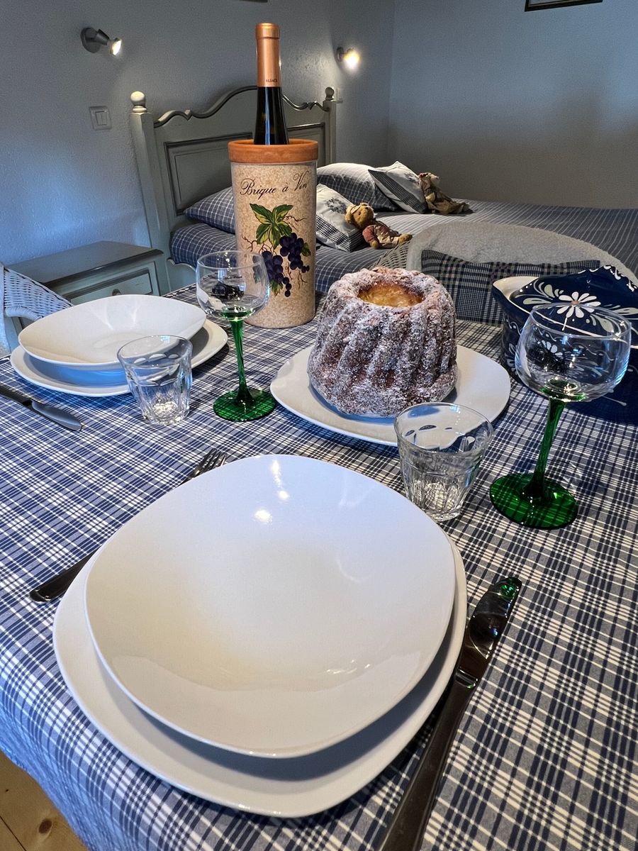 Plongez dans l’ambiance alsacienne ! Voici une table joliment dressée, avec un délicieux Kougelhopf et une bouteille de vin local. Profitez du charme authentique de Kaysersberg dans un cadre chaleureux et typique.